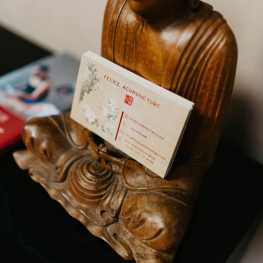 A Felice Acupuncture business card on a carved wooden Buddha