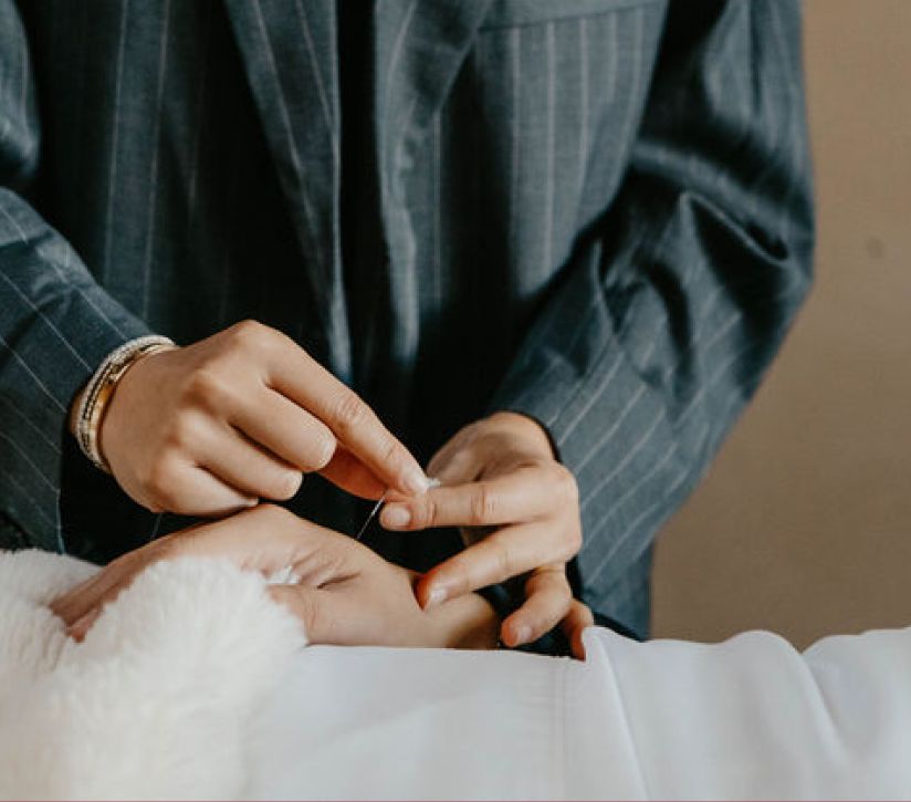 A practitioner placing a fine acupuncture needle in a patient’s wrist